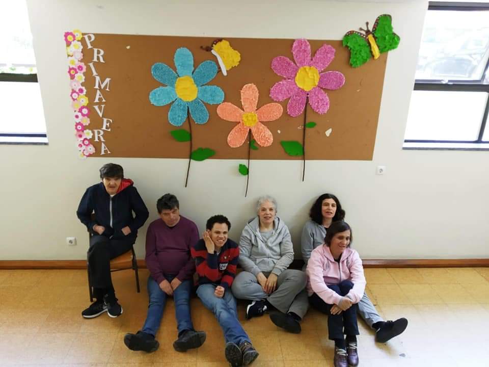Seis clientes do lar residencial Alecrim junto a três flores coloridas afixadas num placar na paredee
