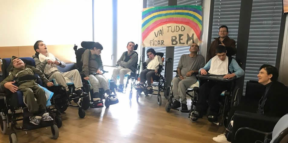 Nove clientes do lar residencial da Associação de Paralisia Cerebral de Guimarães com a faixa "Vai tudo ficar bem" e o arco-íris pintado 